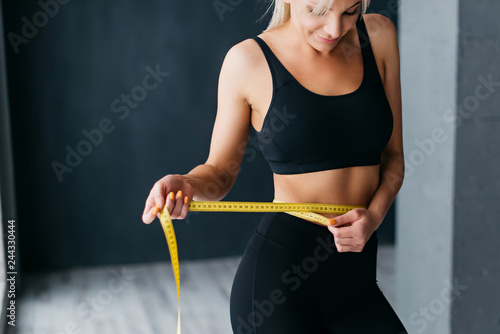 Athletic slim woman measuring her waist by measure tape