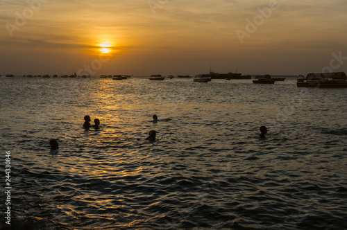 Beautiful view of the silhouettes of the children playing in the sea making splashes of the water lit by sunset backlight.Silhouette of a children. Stone Town, Zanzibar, Tanzania.