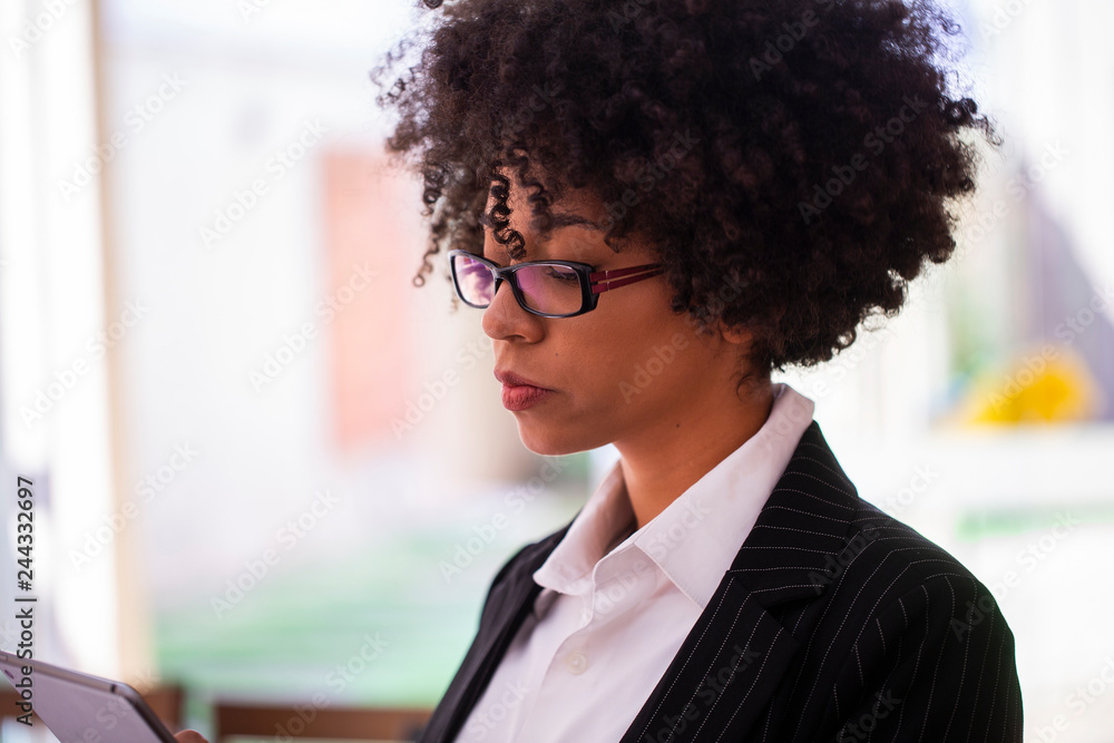 Successful young African American businesswoman looking focused while working on a digital tablet in her home office Successful young African American businesswoman looking focused while working on a digital tablet in her home office