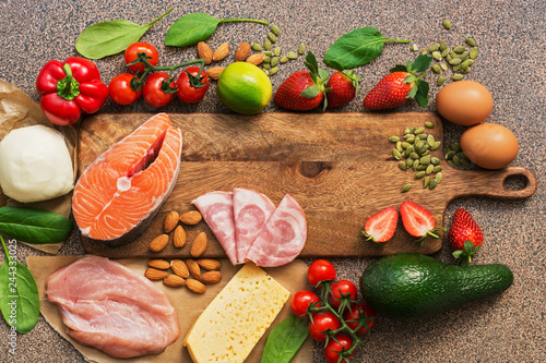 Healthy foods low in carbohydrates. Keto diet concept. Salmon, chicken, vegetables, strawberries, nuts, eggs and tomatoes, cutting board. Top view.
