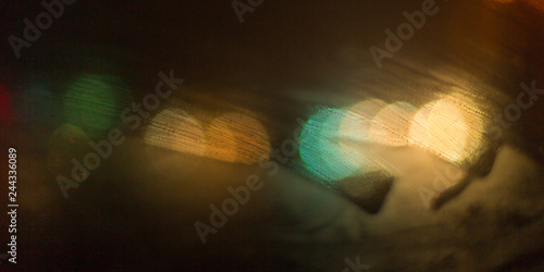 condensate on a transparent glass window and bokeh lights from cars and a red traffic light, on a rainy night view from the car inside