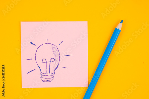Bulb drawn with blue pencil on pink sticker on yellow background. Concept of creative thinking