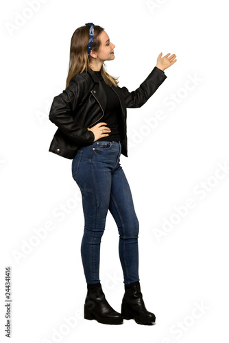 A full-length shot of a Teenager girl with leather jacket pointing back and presenting a product on isolated white background