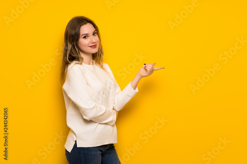 Teenager girl over yellow wall pointing finger to the side in lateral position