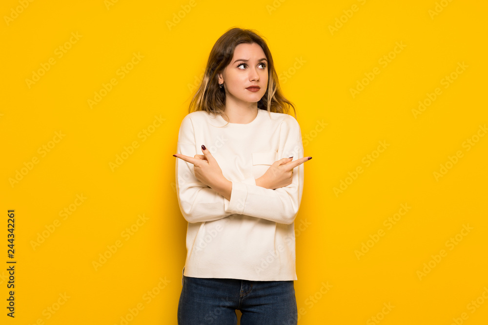 Teenager girl over yellow wall pointing to the laterals having doubts Teenager girl over yellow wall pointing to the laterals having doubts
