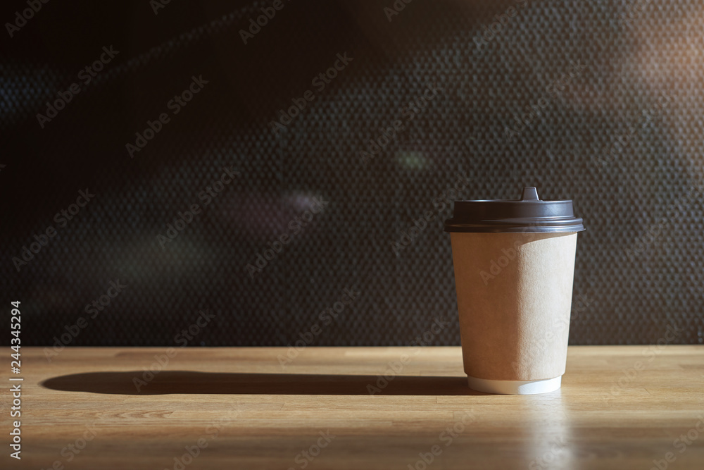Close-up view of disposable paper glass on wooden table in a sunny cafe. Close-up view of disposable paper glass on wooden table in a sunny cafe.