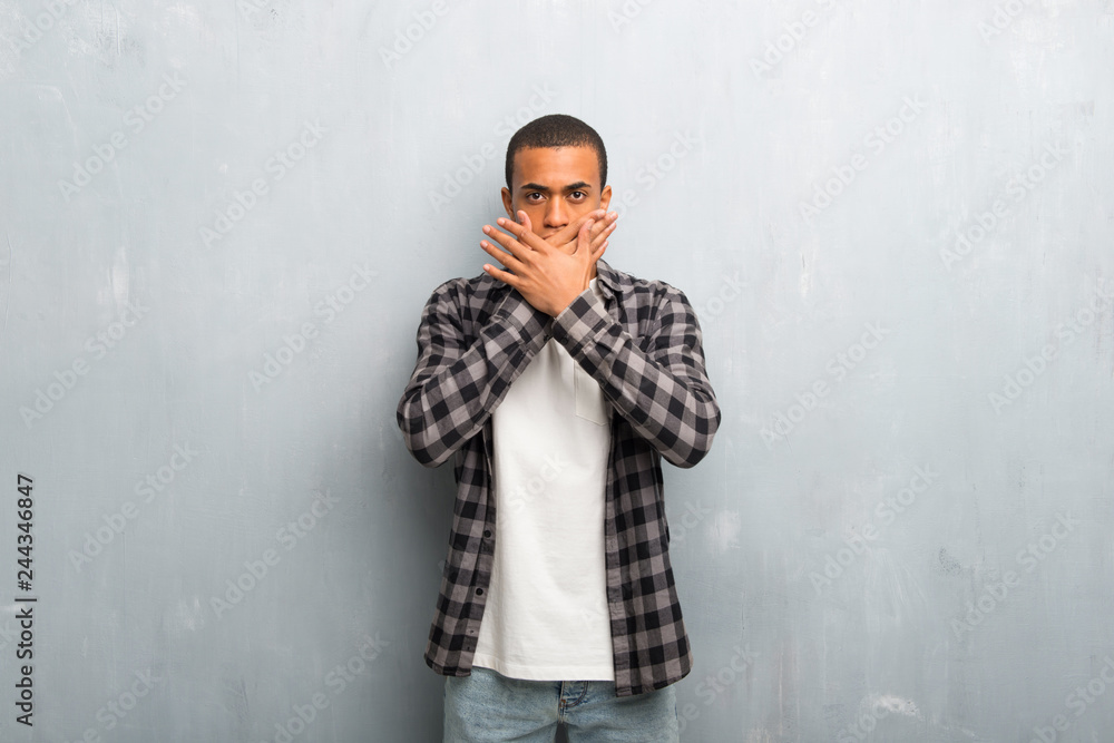 Young african american man with checkered shirt covering mouth with hands for saying something inappropriate Young african american man with checkered shirt covering mouth with hands for saying something inappropriate