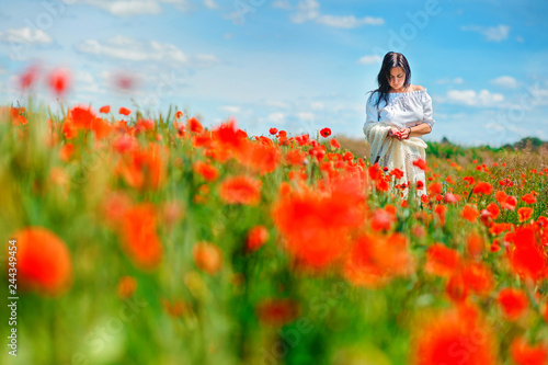 Beautiful girl walks in a poppy field, holding petals in her hands, spring mood