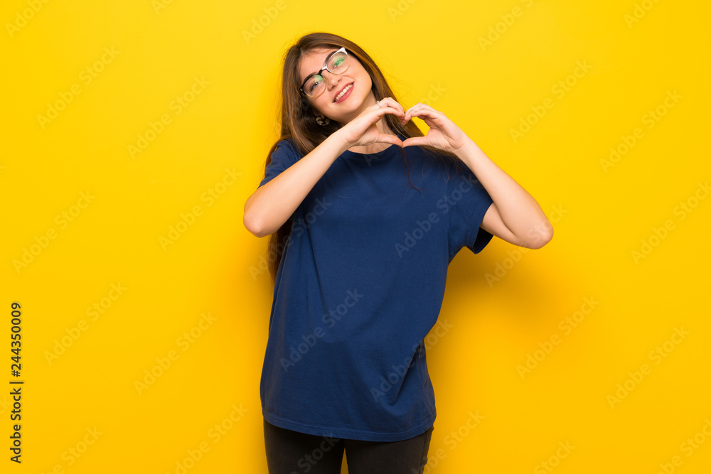 Young woman with glasses over yellow wall making heart symbol by hands Young woman with glasses over yellow wall making heart symbol by hands