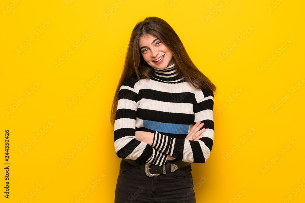 Young woman over yellow wall keeping the arms crossed while smiling Young woman over yellow wall keeping the arms crossed while smiling