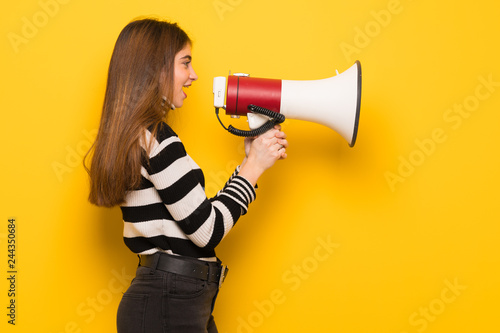 Young woman over yellow wall shouting through a megaphone to announce something in lateral position
