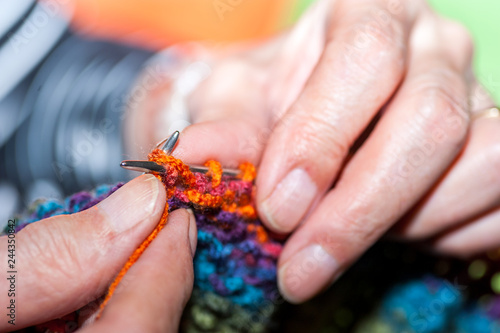 Needlework, Hands of old woman holding knitting needles and multi colored wool for woolwork of warm sweater for cold winter days close up selective focus. Woman knitting sweater.