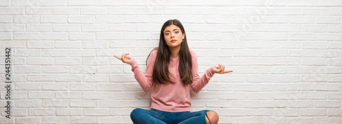 Photos Teenager girl sitting on the floor in a room pointing to the laterals having dou