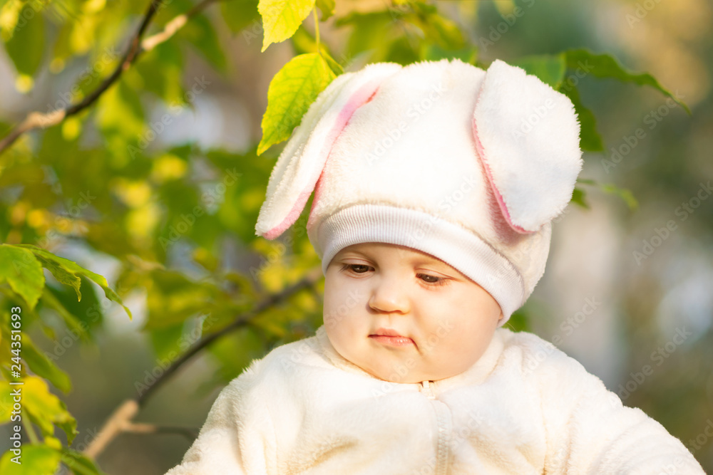 Serious baby in bunny costume seating near tree in park. Serious baby in bunny costume seating near tree in park.