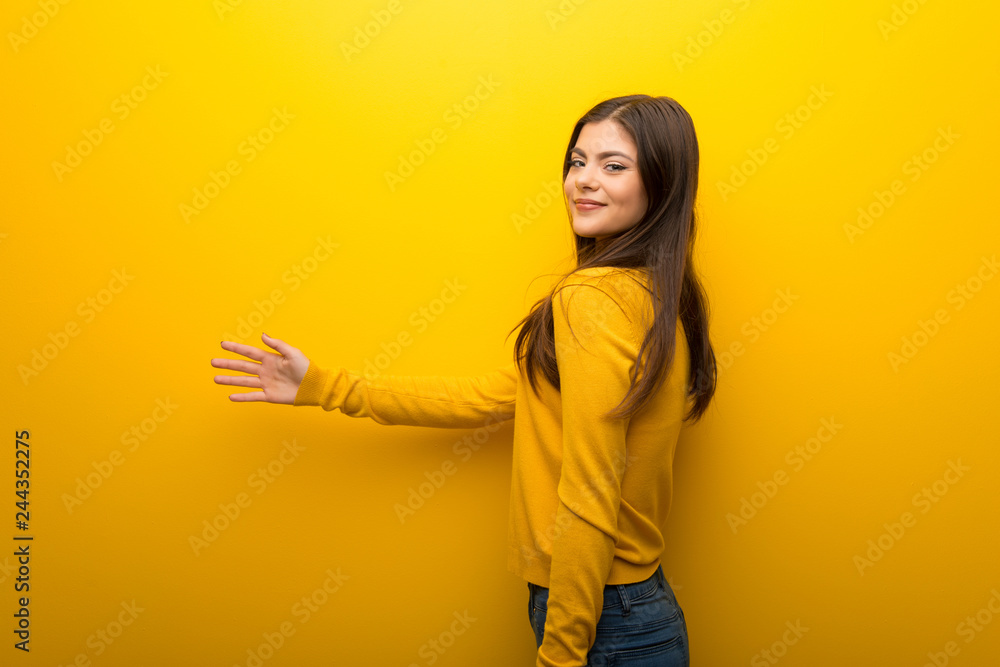 Teenager girl on vibrant yellow background handshaking after good deal Teenager girl on vibrant yellow background handshaking after good deal