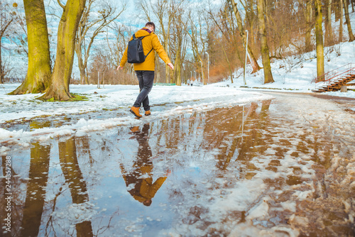 man goes carefully through puddles. spring is coming.