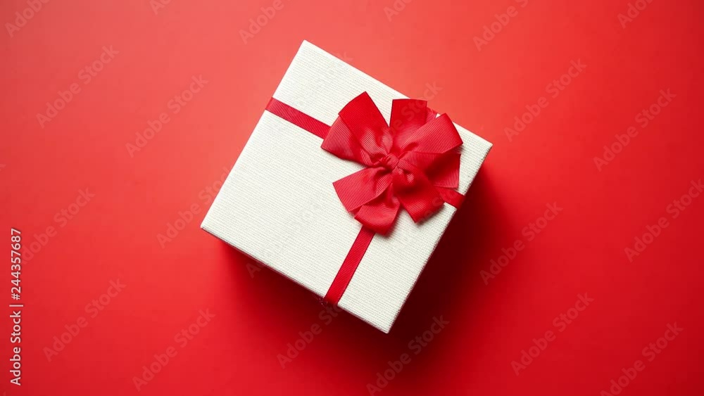 Top view on gift wrapped in striped gift paper decorated with ribbon on red paper background. Valentine, Christmas or Birthday and celebration concept Top view on gift wrapped in striped gift paper decorated with ribbon on red paper background. Valentine, Christmas or Birthday and celebration concept