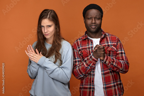 Sly mysterious young woman of Caucasian appearance and her cunning dark skinned boyfriend going to make fun or prank their common friend, squinting eyes and rubbing hands, scheming tricky plan