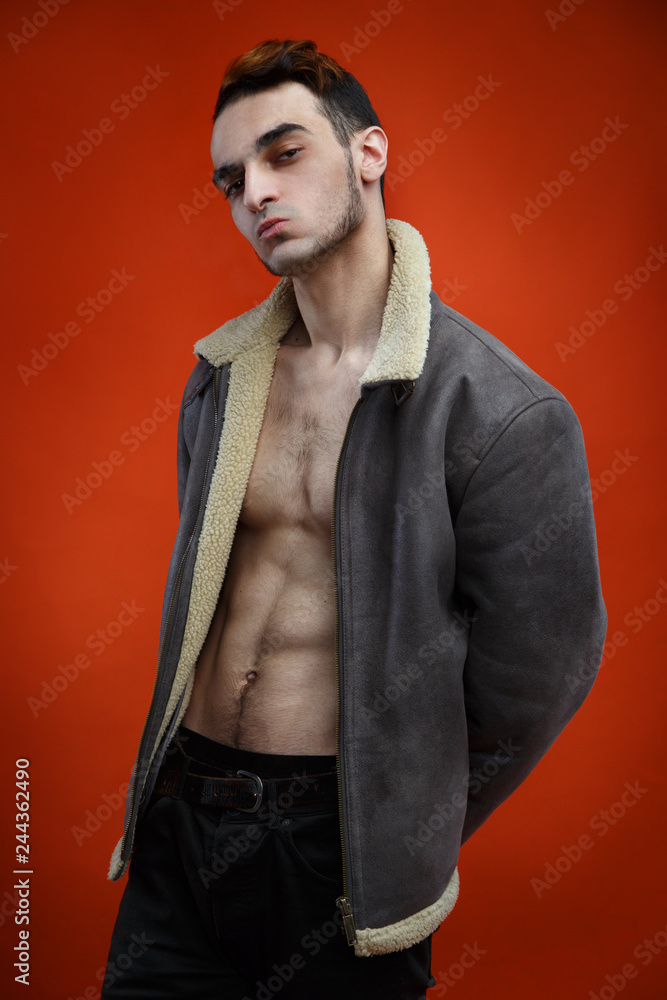 Young hipster guy in a sheepskin coat on a naked body on a red background.