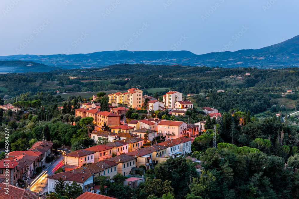 Chiusi village in morning before sunrise in Umbria Italy with illuminated lights on streets and rooftop houses on mountain countryside and rolling hills