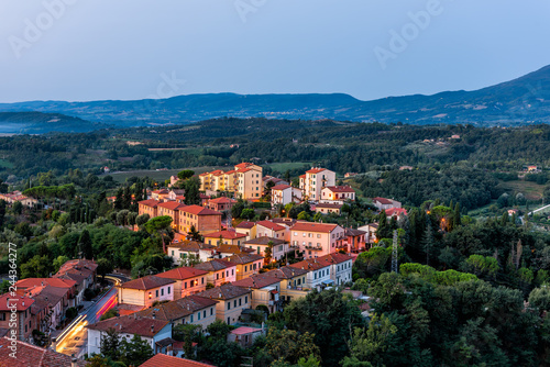 Chiusi village in morning before sunrise in Umbria Italy with illuminated lights on streets and rooftop houses on mountain countryside and rolling hills