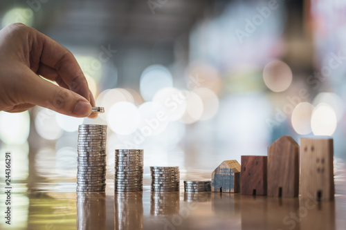Foto Hand choosing row of coin money on wood table and mini wood house, selective focus, Planning to buy property