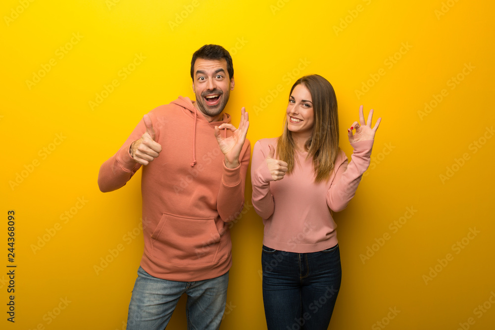 Fototapeta premium Group of two people on yellow background showing ok sign with and giving a thumb up gesture