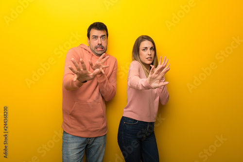 Group of two people on yellow background is a little bit nervous and scared stretching hands to the front