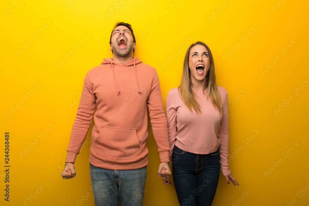 Group of two people on yellow background shouting to the front with mouth wide open Group of two people on yellow background shouting to the front with mouth wide open