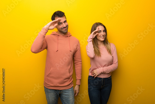 Group of two people on yellow background saluting with hand
