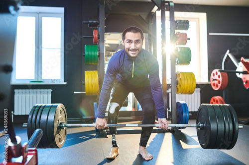 Young athlete with amputee leg standing and raising the bar in health club