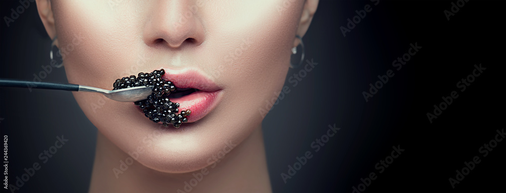 Beautiful fashion model woman eating black caviar. Beauty girl with caviar on her lips isolated on black background - obrazy, fototapety, plakaty 