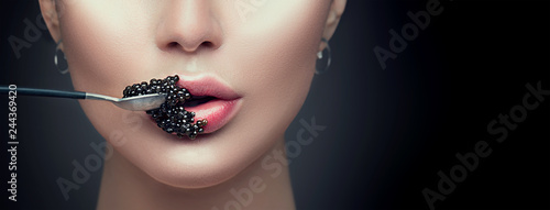 Beautiful fashion model woman eating black caviar. Beauty girl with caviar on her lips isolated on black background