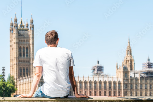 Photography Back of young man with white tshirt sitting on railing in London looking at city