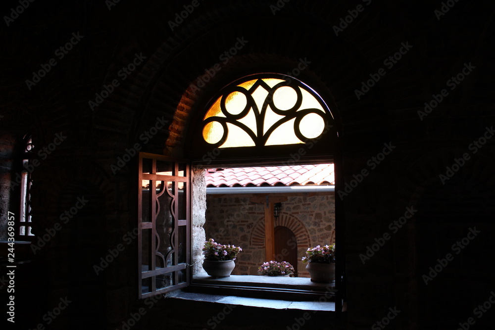 Daylight enters the dark room of the monastery through a small open window with flower pots, wooden frames, thick stone walls, brickwork
