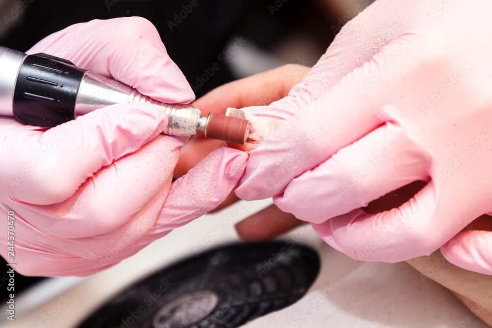 Closeup shot of hardware manicure in a beauty salon. Manicure process, cleaning of nails by a milling cutter. Procedure for the preparation of nails before applying nail polish.