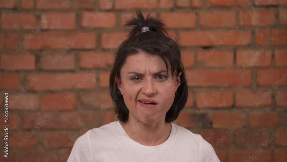 Displeased young woman chewing bubble gum with open mouth isolated against a brick wall background Displeased young woman chewing bubble gum with open mouth isolated against a brick wall background