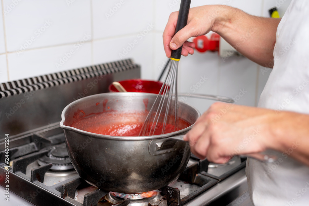 Pastry Chef in the kitchen cooking a red strawberry marmalade cream .