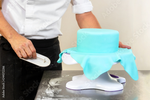 Confectioner decorating a wedding cake with blue fondant .