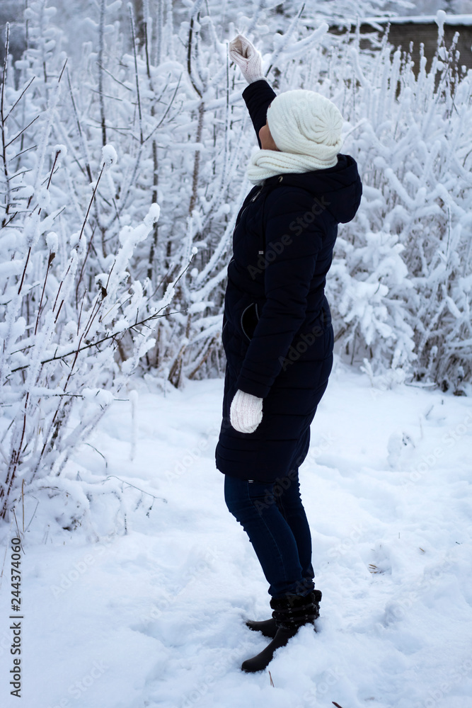 woman in warm winter clothes and in knitted hat enjoying a walk in winter snowy forest