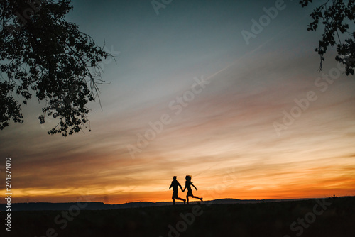 Young couple running by the sea and looking at the sun