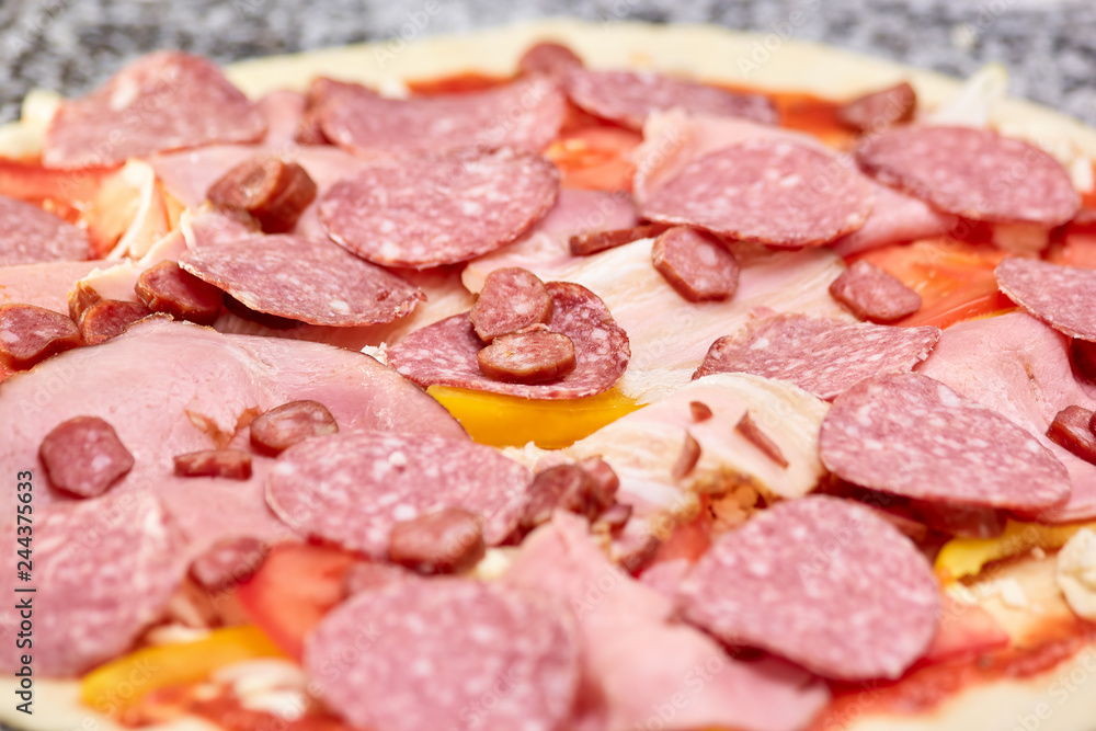 Closeup spicy salami pizza before baking. Large amound of salami and hams on pizza dough.