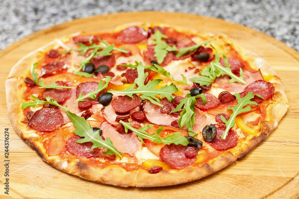 Pepperoni pizza with arugula. Tasty pizza with vegetables and arugula on round wooden board.