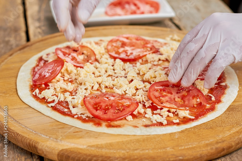 Adding tomatoes to pizza. Chef hands putting sliced tomatoes on uncooked pizza.