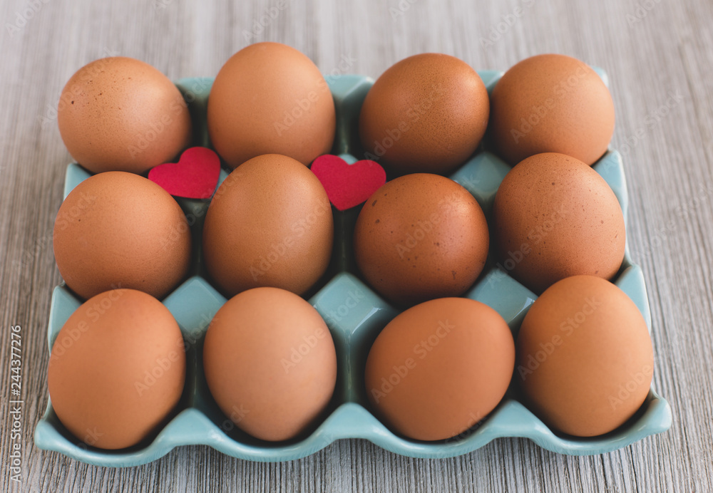 Organic Brown Chicken eggs in a Blue Plastic Box Decorated Two Red Heartson a Wooden Table . Close up. Easter Concept.