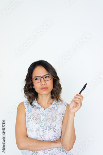 Frowning Asian trainee concerned and puzzled. Young woman wearing glasses, holding pen, and looking away. Problem solving concept