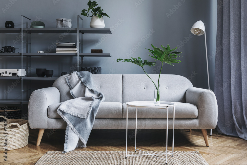 Modern nordic living room with design sofa with elegant blanket, coffee  table,white lamp and bookstand on the grey wall. Brown wooden parquet.  Concept of minimalistic interior. Stock-Foto | Adobe Stock