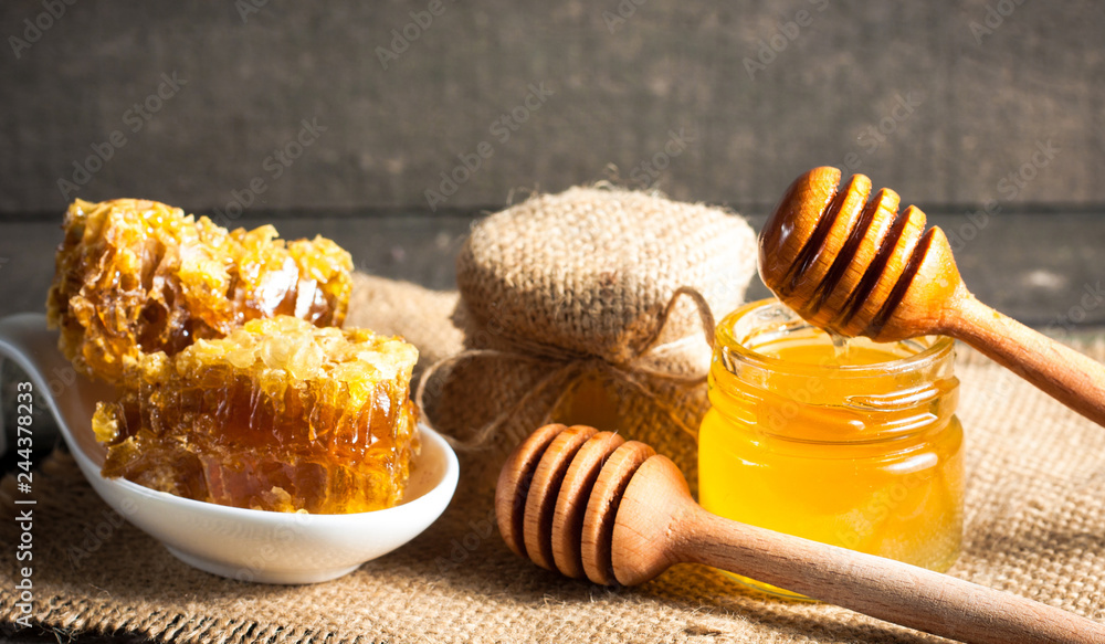 Honey dripping from a wooden honey dipper in a jar on wooden grey rustic background Honey dripping from a wooden honey dipper in a jar on wooden grey rustic background