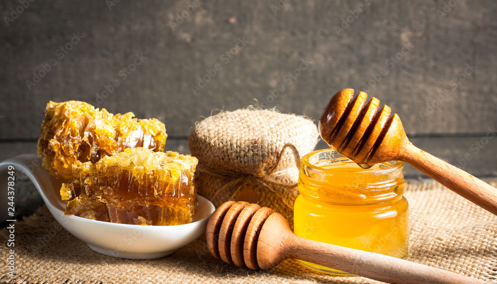 Honey dripping from a wooden honey dipper in a jar on wooden grey rustic background Honey dripping from a wooden honey dipper in a jar on wooden grey rustic background