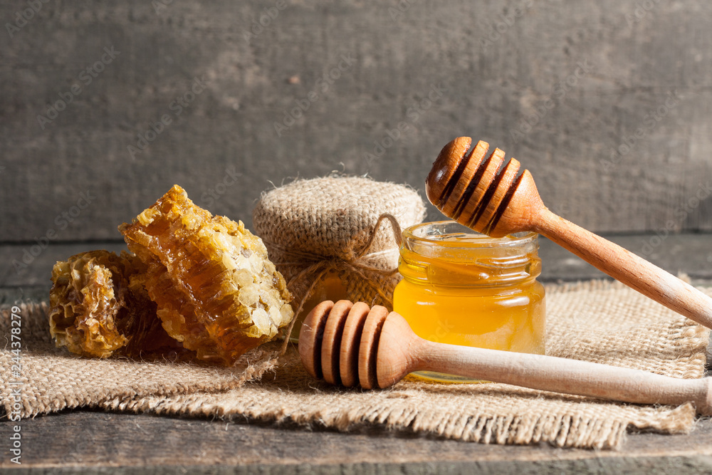 Honey dripping from a wooden honey dipper in a jar on wooden grey rustic background Honey dripping from a wooden honey dipper in a jar on wooden grey rustic background